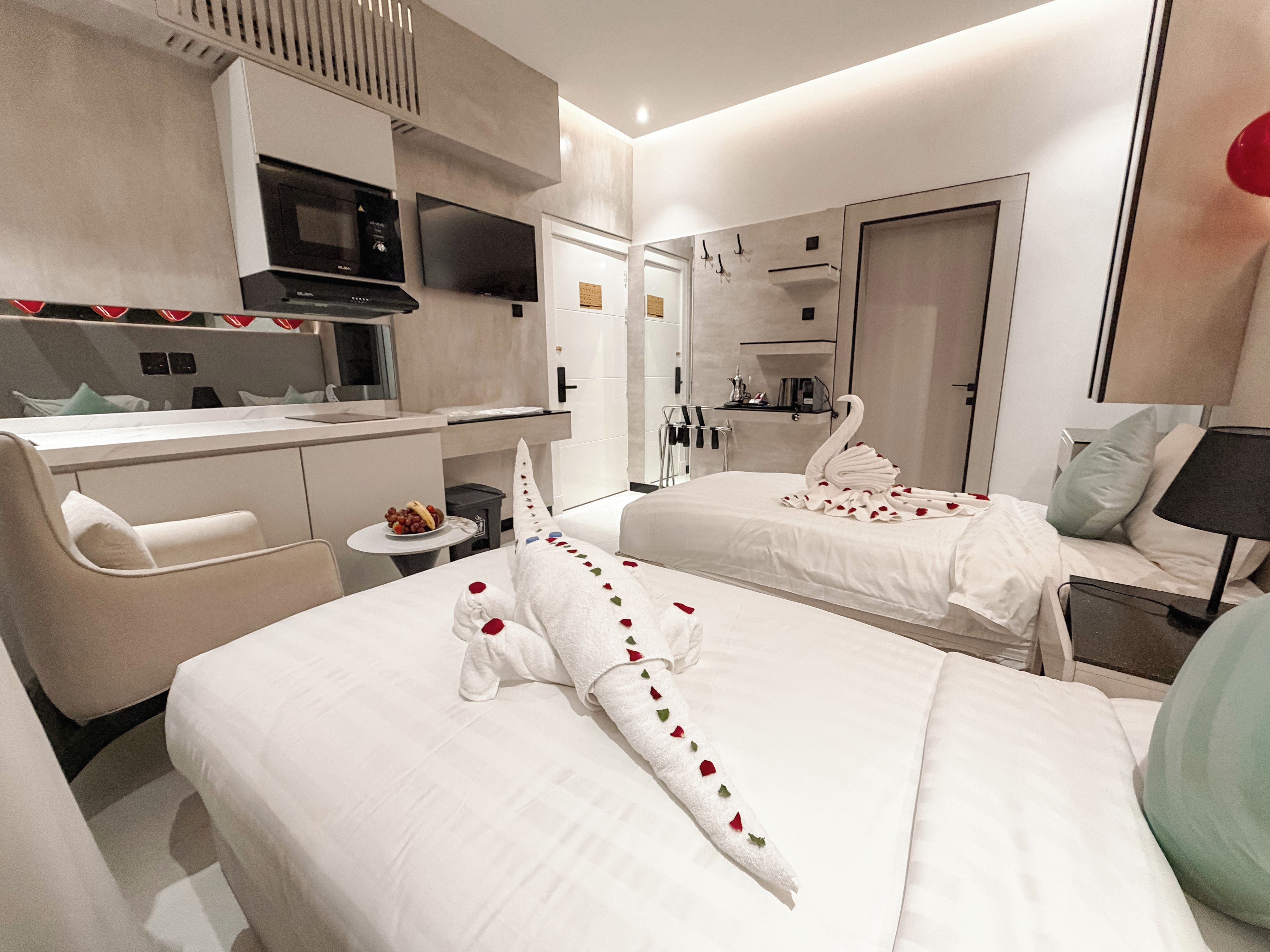 A hotel room with a kitchenette, two beds, a sofa, and a TV.