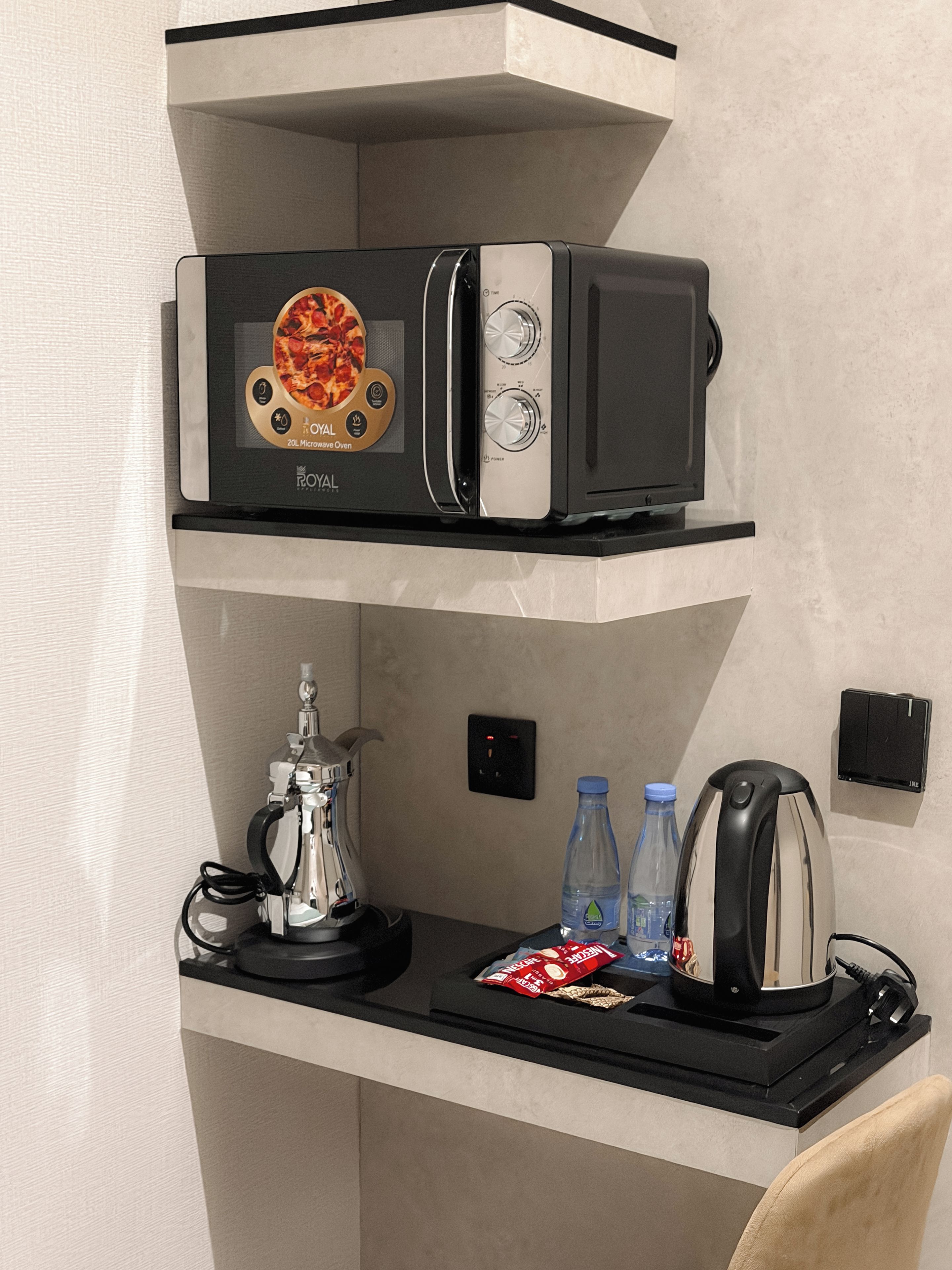 A microwave oven with a pizza image on the front, a coffee maker, two water bottles, and a kettle on a countertop.