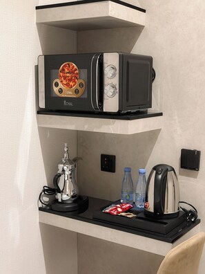 Un horno microondas con una imagen de pizza en la puerta, una cafetera, dos botellas de agua y una tetera sobre una encimera.