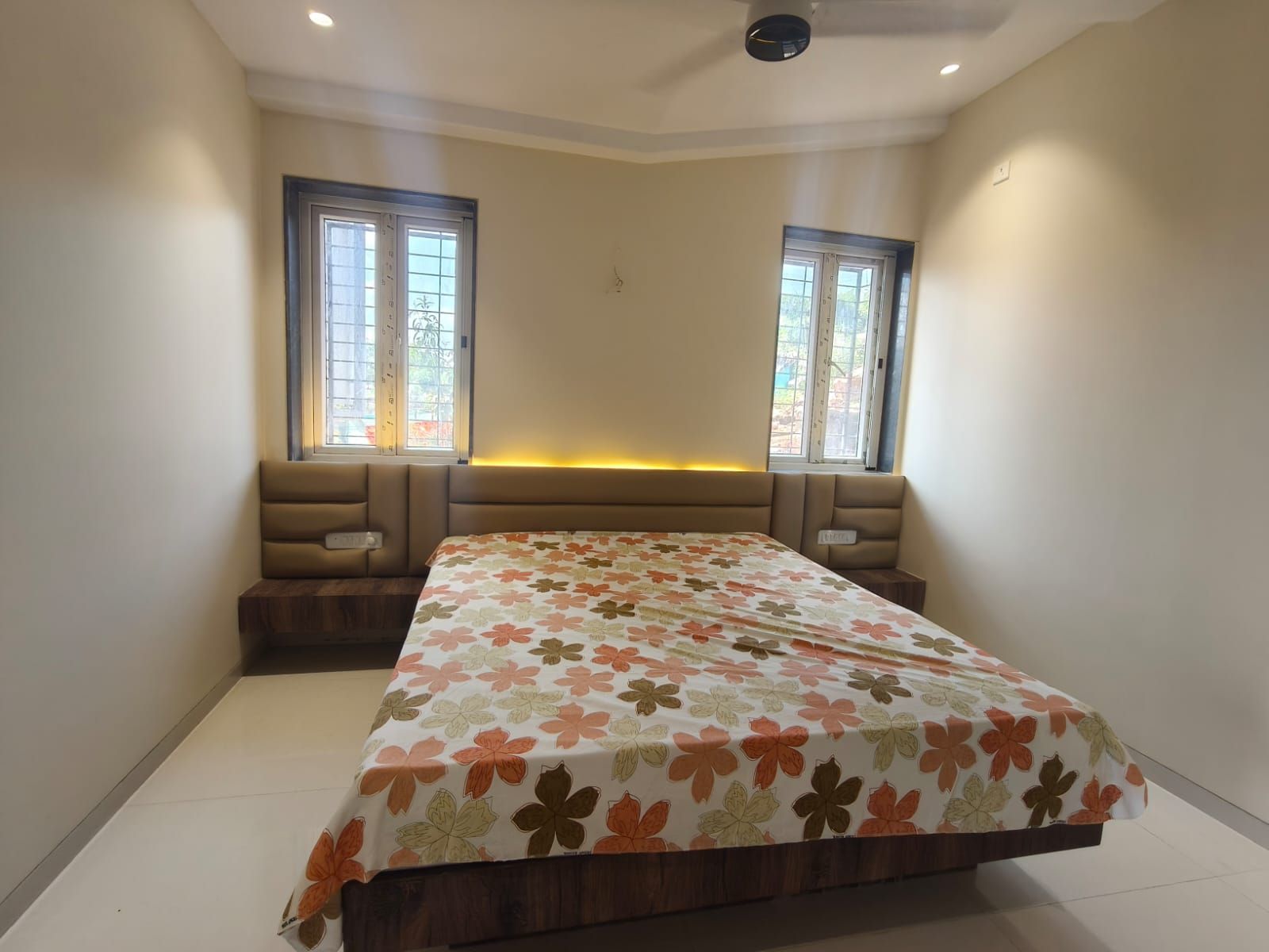 Une chambre à coucher avec un lit, deux fenêtres, un ventilateur de plafond et un banc.