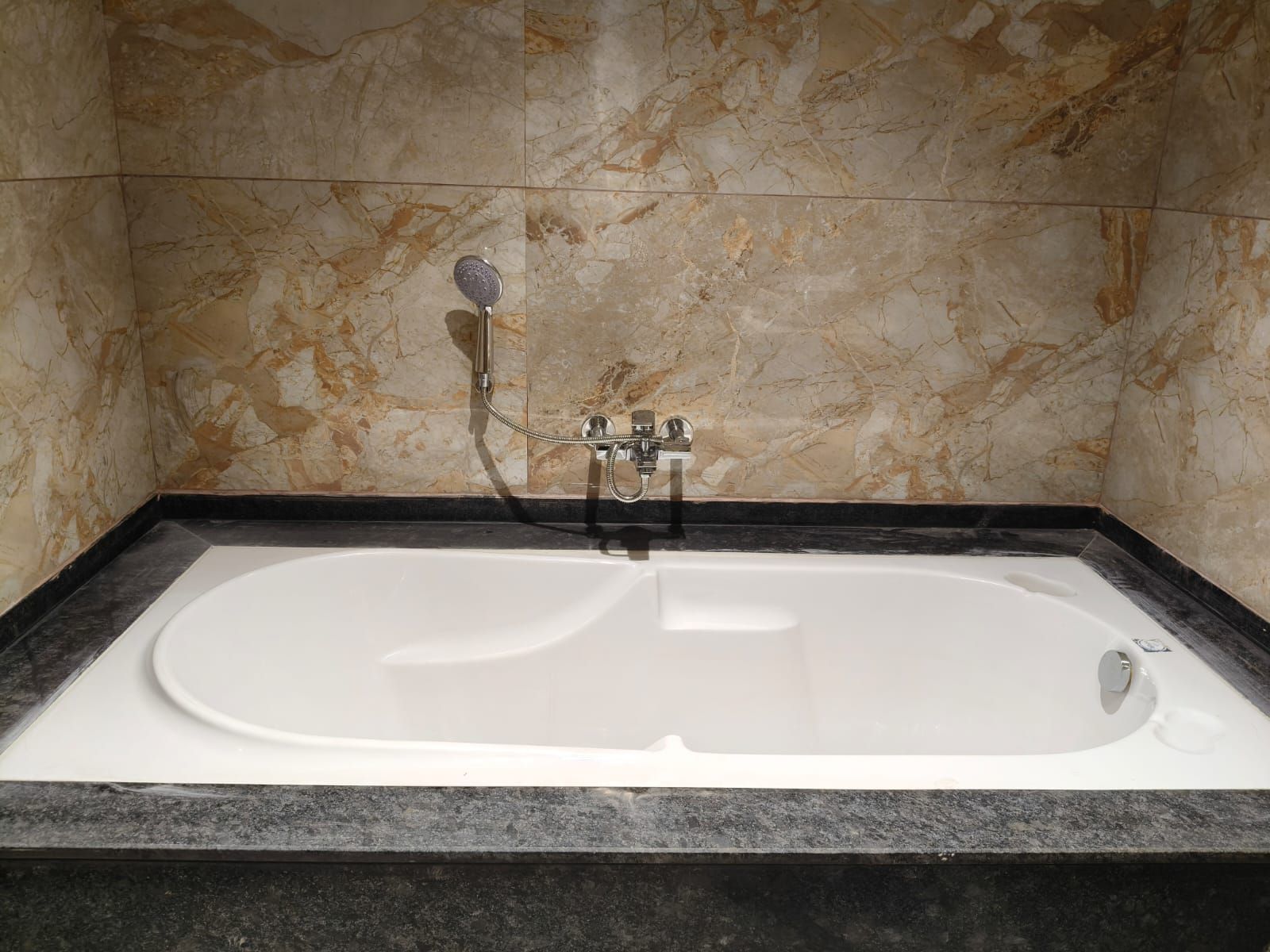 Banyera rectangular amb plat de dutxa i panell de control, davant d'una paret de marbre.