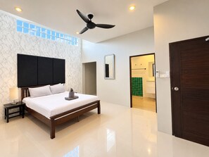 A modern hotel room with a bed, a ceiling fan, a nightstand, a mirror, and a view of the bathroom. - 10 bedroom & bath. 2 pools villas for 28 guests. (Tambon Kathu)
