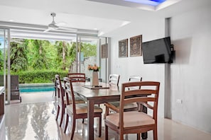A modern dining area with a glass wall, a ceiling fan, and a flat-screen TV on the wall. - 10 bedroom & bath. 2 pools villas for 28 guests. (Tambon Kathu)