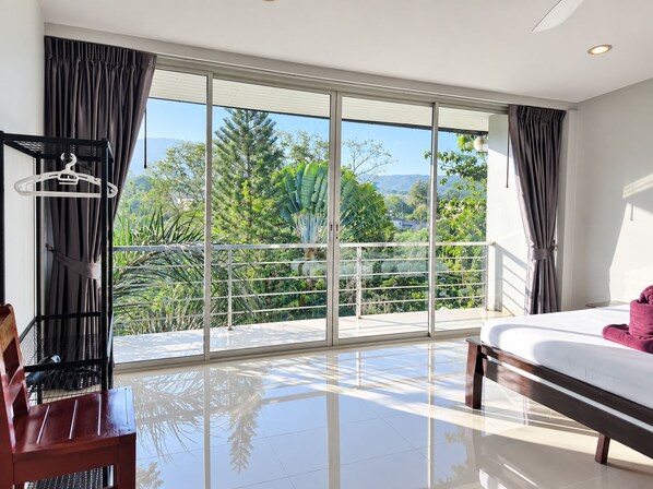 Ein Hotelzimmer mit einer großen Schiebeglasdoor zum Balkon mit Blick auf Grünflächen und Berge.