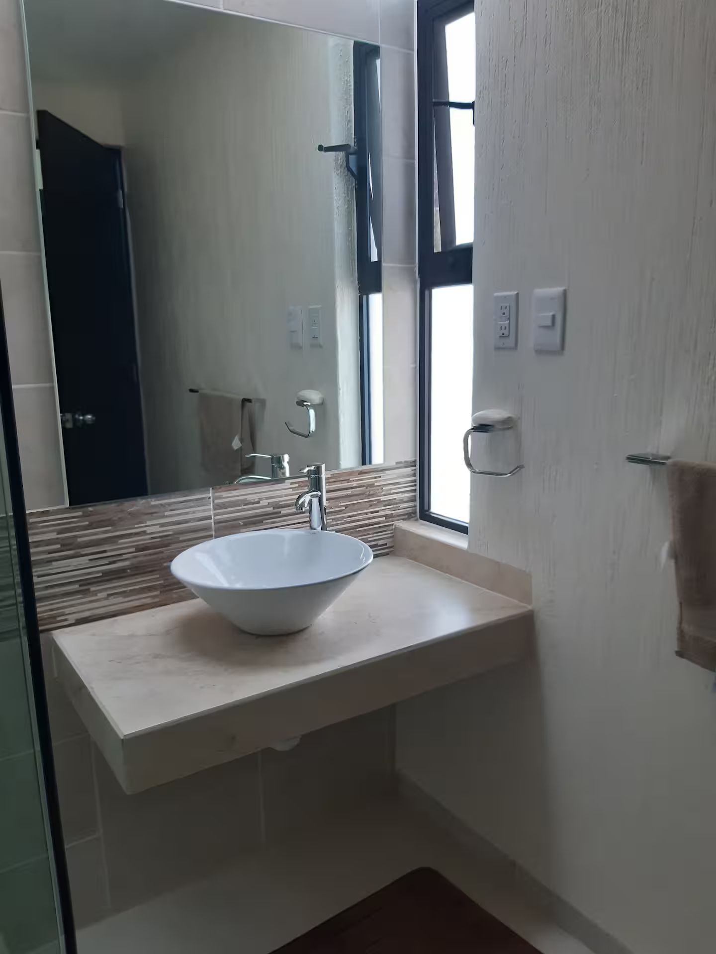 Une salle de bain avec un lavabo blanc, un miroir et une fenêtre.