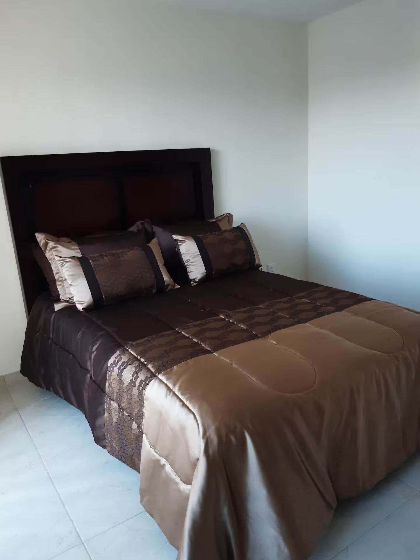 A bed with a dark headboard, multiple pillows, and a light-colored bedspread.
