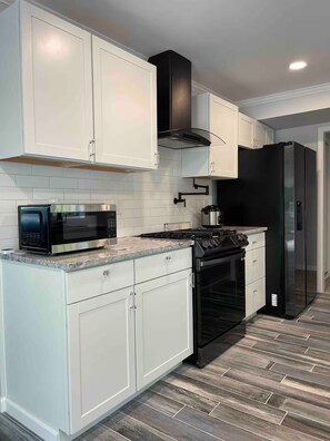 A modern kitchen with white cabinetry, a black stove, a microwave, and a refrigerator. - Mia's House (Radcliff)