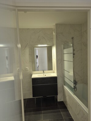 A bathroom with a white sink, a mirror, a shower, and dark tiled flooring. - Spacious 4-room apartment near Paris and Orly Airport (Châtenay-Malabry)