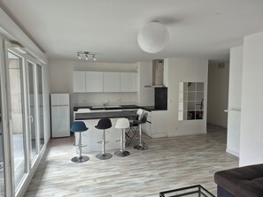 A modern kitchen with white cabinets, a black countertop, and a central island. There are three bar stools with metal legs and white seats. A large white pendant light hangs from the ceiling. - Spacious 4-room apartment near Paris and Orly Airport (Châtenay-Malabry)