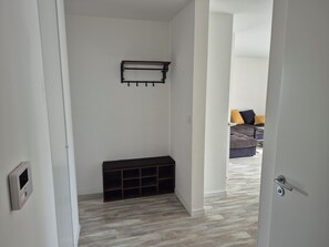 A hallway with a bench, a coat rack, and a door leading to a living area with a couch and pillows. - Spacious 4-room apartment near Paris and Orly Airport (Châtenay-Malabry)
