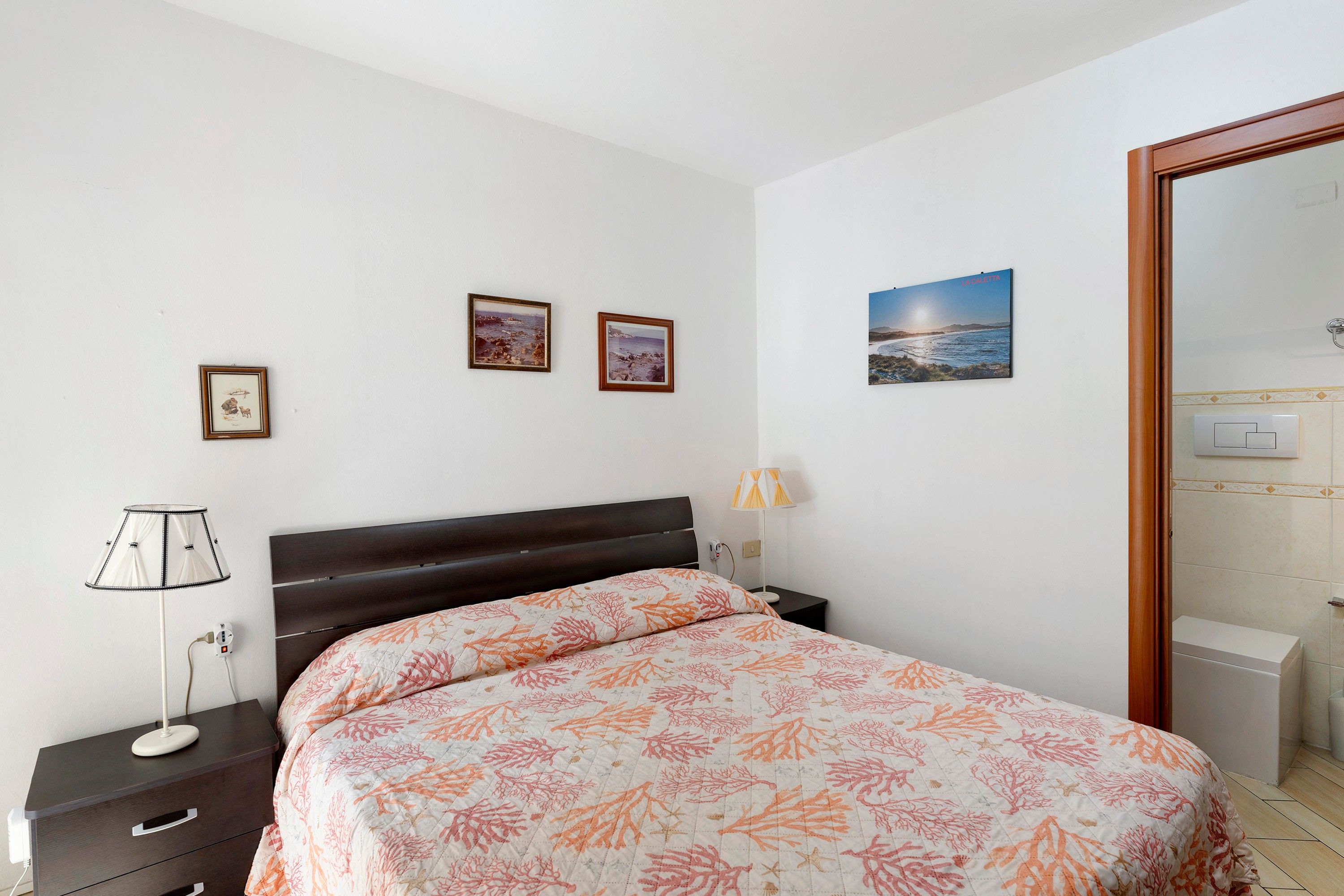 Ein Schlafzimmer mit einem Bett, Nachttisch, Lampe und Bildern an der Wand.