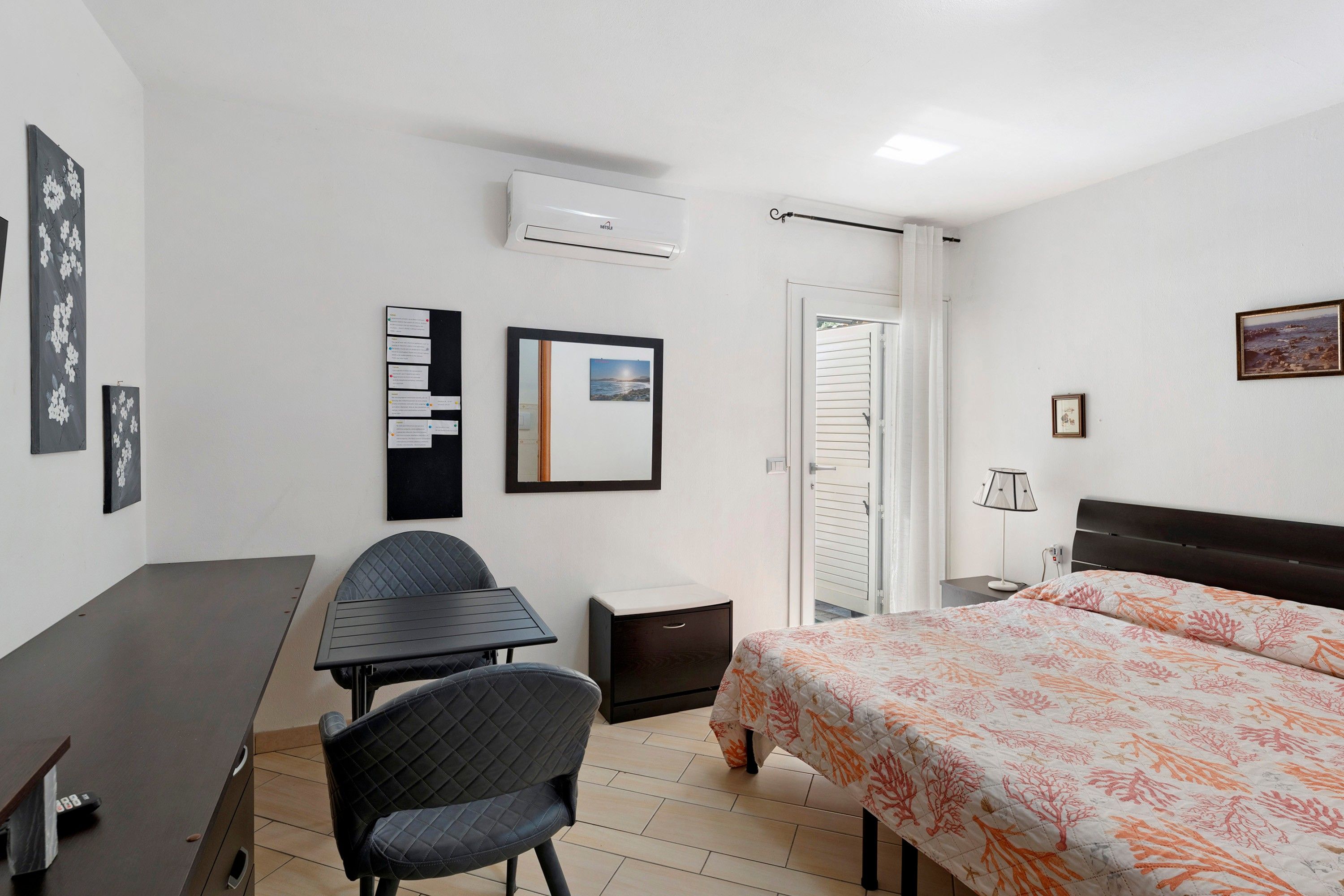 Ein Hotelzimmer mit Bett, Schreibtisch, Stuhl, kleinem Tisch, Nachttisch, Klimaanlage, einer Tür und einem Fenster.