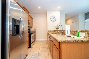 A modern kitchen with stainless steel appliances, wooden cabinets, a granite countertop, and a wall-mounted clock. - 5BR Paradise Palms Toy Story & Minions Rooms (Kissimmee)