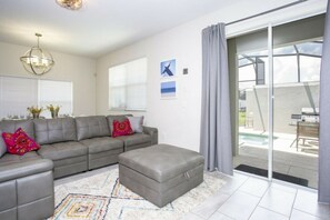 Ein modernes Wohnzimmer mit einem grauen Sofa, einem Hocker und einem gemusterten Teppich.