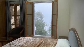 A bedroom with a bed, a chair, a table, and a window with curtains.