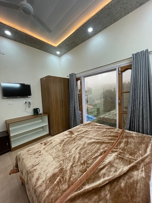 A bedroom with a bed, a TV, a wardrobe, and a window with curtains.