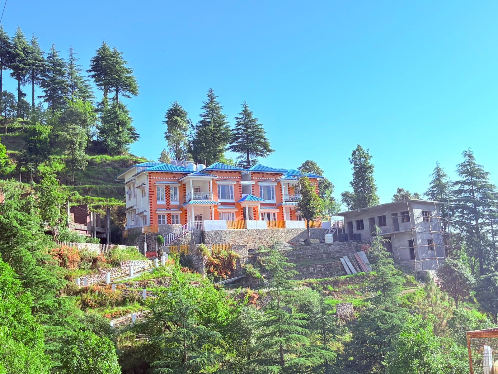 A multi-story building with a red and white facade, situated on a hillside with dense forest.