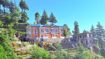 A multi-story building with a red and white facade, situated on a hillside with dense forest.