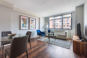 Ein modernes Wohnzimmer mit einem Glastisch, einer Couch, einem blauen Sessel und einem großen Fenster mit Jalousien.