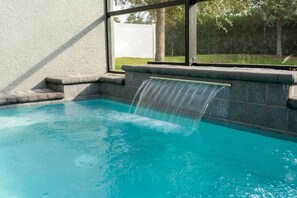 A swimming pool with a waterfall feature, surrounded by a stone wall and a window. - 4BR near Disney | Private pool, themed rooms (Kissimmee)