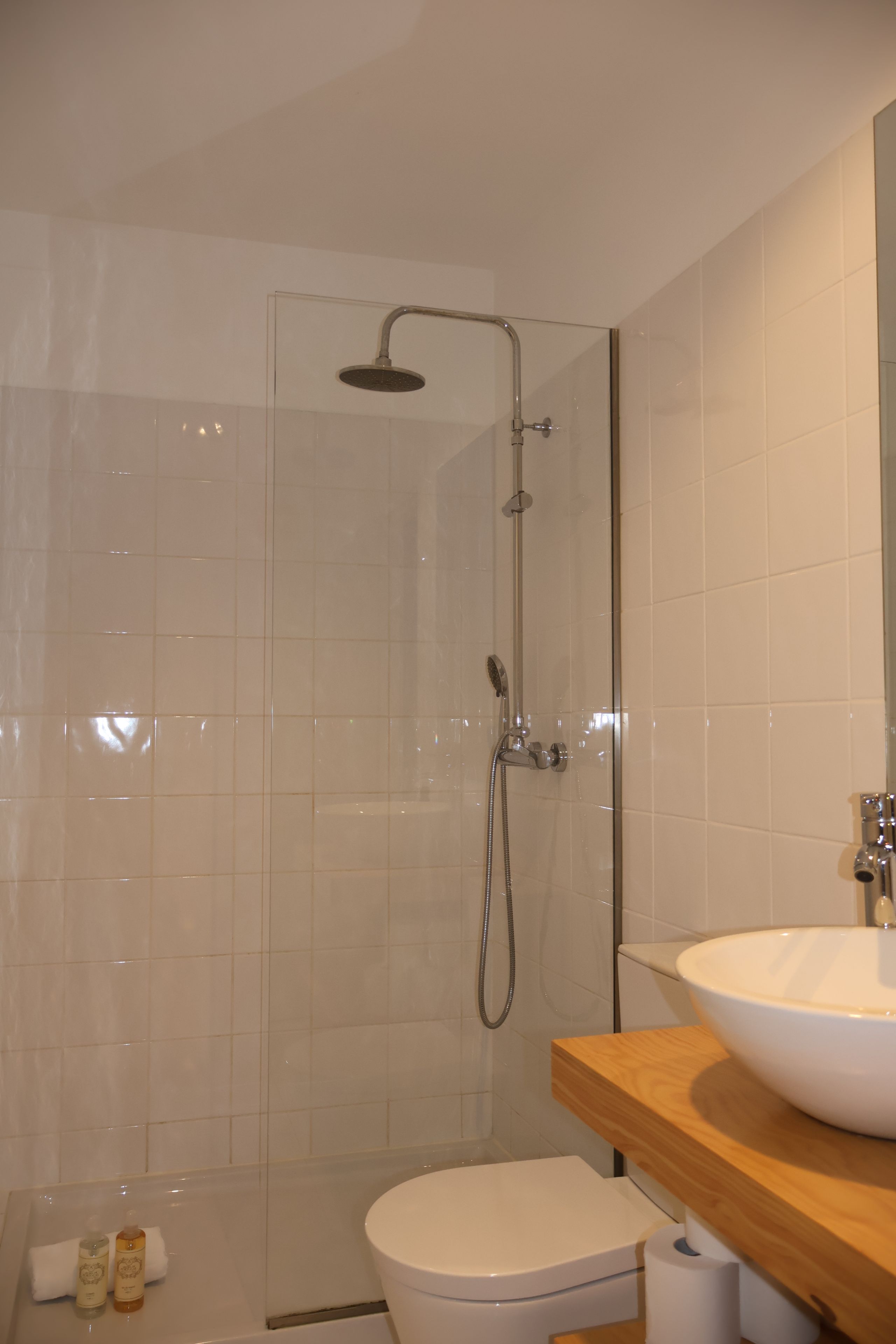 Een moderne badkamer met een douchecabine van glas, een wit toilet en een houten wastafelmeubel met een witte wastafel.