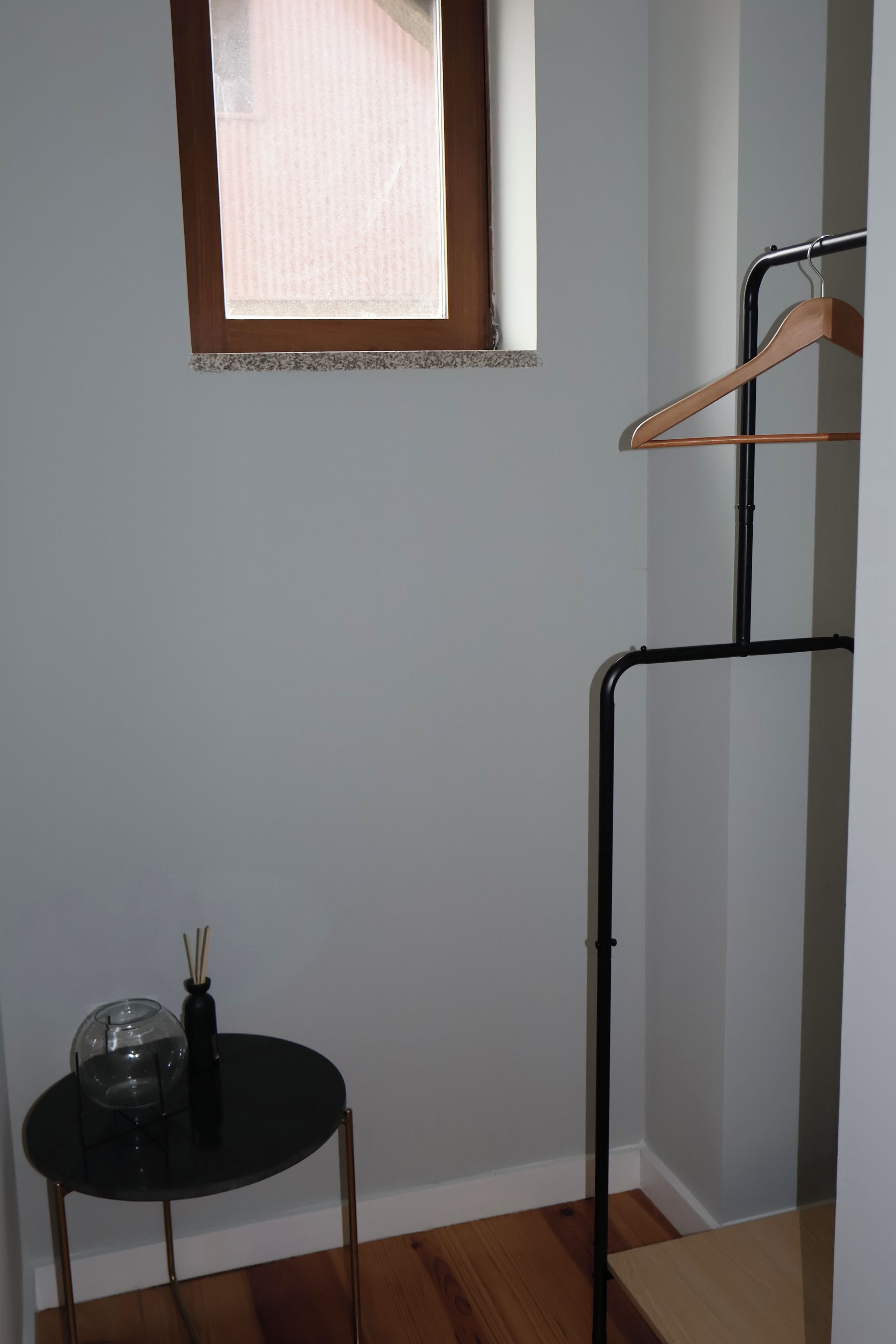 A room with a small table, a hanging clothes rack, and a window.