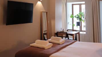 Habitación de hotel con cama, televisor de pantalla plana en la pared, escritorio con silla, ventana con cortinas y planta colgante.