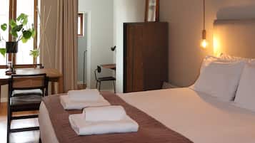 Ein Hotelzimmer mit einem großen Bett, einem Schreibtisch, einem Sessel, einer Pflanze und Blick auf den Flur.