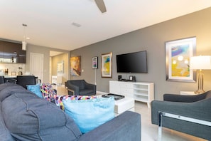 A modern living room with a grey sofa, a coffee table, and a TV. There is a white cabinet and artwork on the walls. - 4BR Le Reve townhome | Pool & themed rooms (Kissimmee)