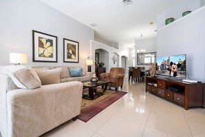 A spacious living room with a sofa, armchair, coffee table, and a television. - 4BR Windsor Palms | Pool, spa & Mickey room (Kissimmee)