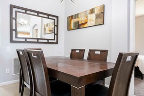 A dining room with a rectangular table and six chairs, a large mirror, and a painting on the wall. - 4BR Windsor Palms | Pool, spa & Mickey room (Kissimmee)