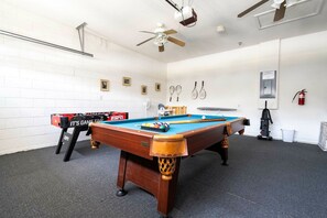 A pool table with a foosball table and a ceiling fan in a room with white brick walls. - 4BR Windsor Palms | Pool, spa & Mickey room (Kissimmee)