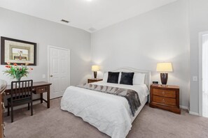A bedroom with a bed, two bedside tables, a desk, a chair, a door, and a framed picture on the wall. - 4BR Windsor Palms | Pool, spa & Mickey room (Kissimmee)
