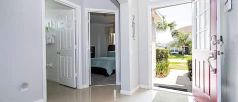 A hallway with a red door leading to a bedroom with a bed and a window.