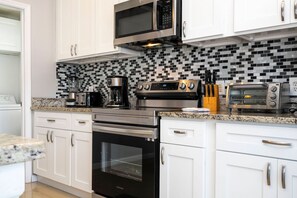 A modern kitchen with white cabinetry, a black oven, a microwave, a coffee maker, a toaster, and a tiled backsplash. - 4BR Windsor Palms | Pool, spa & Mickey room (Kissimmee)