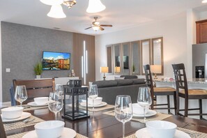 A dining area with a table set for four, a sofa, and a television on the wall. - 4BR townhome near Disney | Pool & Mickey room (Kissimmee)
