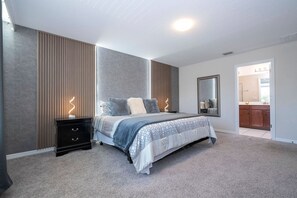 Une chambre à coucher avec un lit, des tables de chevet, un miroir et une vue sur la salle de bain.