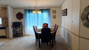 Zona de menjador amb taula preparada per a quatre, un lampadari i vista a través d'una finestra amb cortines de transparència.