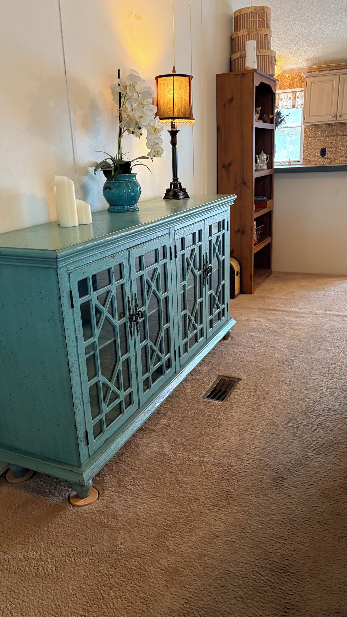 Un mueble color turquesa con puertas de cristal y una pequeña rejilla en la parte inferior.