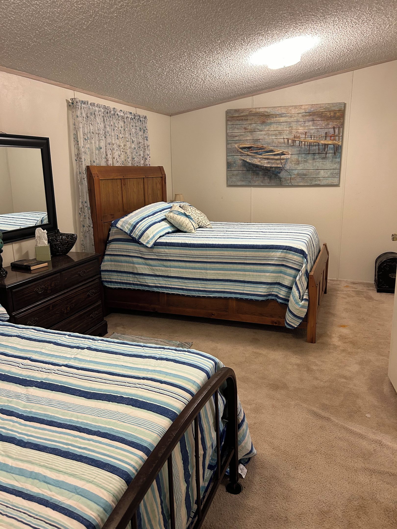 A bedroom with two beds, a wooden headboard, a painting of a boat, a mirror, and a dresser.