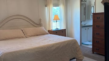 Un dormitorio con cama, ventilador de techo, mesita de noche, cómoda y ventana con cortinas.