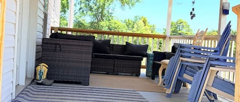 A covered porch with a wicker sofa, a bench, and blue lounge chairs.