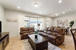 A living room with two leather sofas, a coffee table, and a TV stand. - 5BR townhome near Disney | Pool, themed rooms (Kissimmee)
