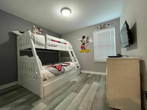 Quarto com beliche, pequeno armário, televisão na parede e janela com persianas.