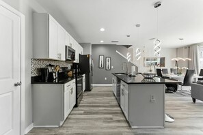 A modern kitchen with white cabinetry, a black countertop, and a dining area with a table and chairs. - 4BR townhome, private pool | Mickey & Star Wars (Kissimmee)