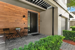 Un área de estar moderna al aire libre con un muro de madera, una puerta negra y un pequeño jardín.