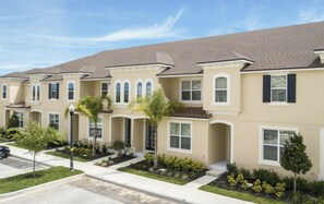 A row of townhouses with a uniform architectural style, featuring a flat roof, a light-colored facade, and a symmetrical window arrangement. - 5BR Solara home | Private pool & themed rooms (Kissimmee)