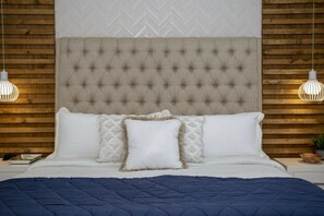 Une chambre à coucher avec une tête de lit capitonnée, du linge de lit blanc et deux lampes de chevet.