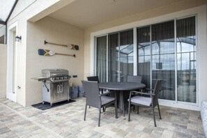 A patio with a grill, wicker chairs, and a glass door leading to a covered area. - 5BR Solara home | Private pool & themed rooms (Kissimmee)