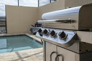 Churrasqueira de aço inoxidável com quatro queimadores e termômetro embutido, ao lado de uma piscina.